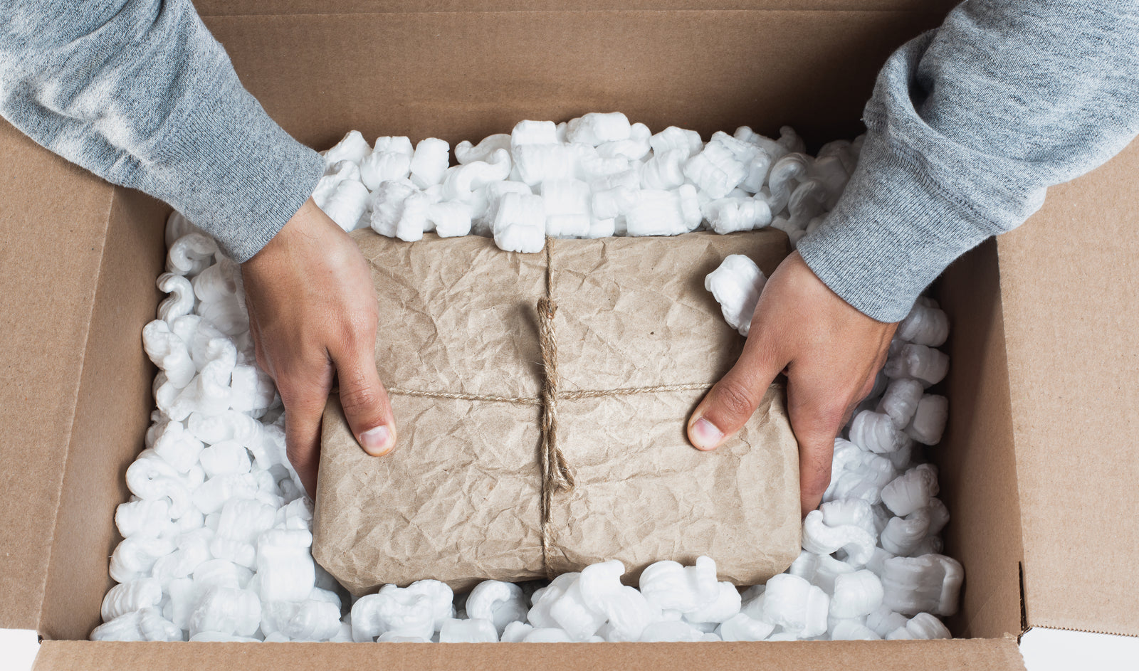 Hands placing a wrapped bundle into a box of packing material